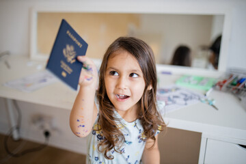 Fototapeta na wymiar Happy little girl in front of a desk and a mirror shows an American passport
