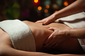 Fototapeta premium Close up of therapist doing stomach massage on woman in spa against dark background.