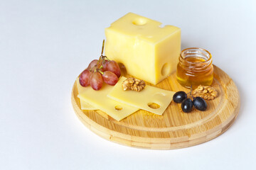 Still life with delicious Emmental cheese on a cutting board with grapes, honey and walnut. Healthy organic products. Copy space, close-up, mock up