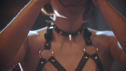 Sexy woman in a leather bondage puts on a studded collar