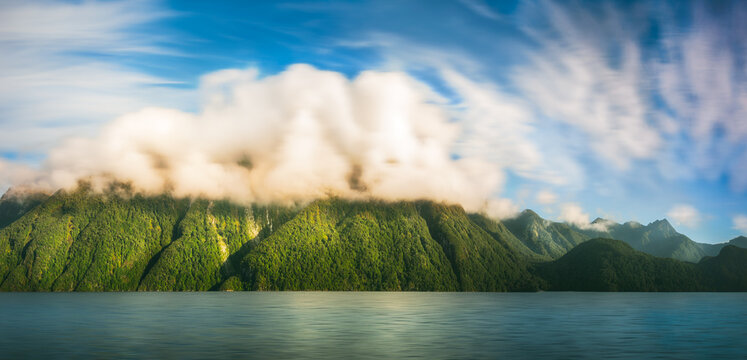 Amazing cloud formation raising over the mountain range at Lake Manapouri early in the morning on an adventure cruise to Doubtful Sound in Fiordland National Park, New Zealand.