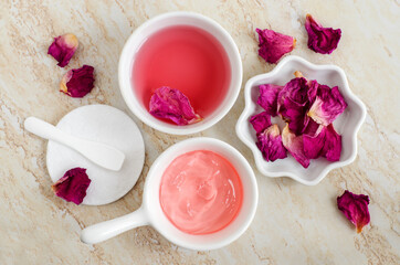 Two small white bowls with rose water (toner) and jelly rose mask. Dry rose petals and cotton pad. Ingredients for preparing homemade cosmetics. Natural beauty treatment recipe, zero waste concept. To