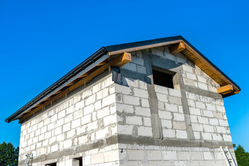 Construction of a small house made of white brick, visible gable roof with boarding and gutter system.