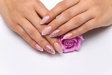 Extension of nails. Wedding french white manicure with painted flowers on sharp long nails holding a pink rose. Close-up on a white background.
