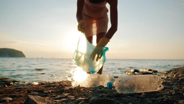 Volunteer girl collects trash in the trash bag. Plastic bottles and other trash on sea beach. Environmental pollution and ecological problem concept.