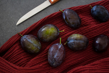 Fresh plums on red textured background. Top view photo of kitchen table. Autumn mood picture. Fresh plums on red textured background. Top view photo of kitchen table. Autumn mood picture. 