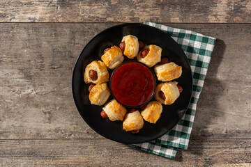 Pigs in blankets. Mini sausages wrapped in puff pastry with ketchup sauce on wooden table