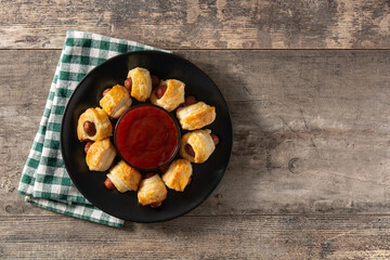 Pigs in blankets. Mini sausages wrapped in puff pastry with ketchup sauce on wooden table
