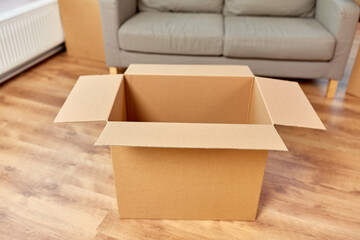 storage, moving and packing concept - empty corrugated box and sofa at new home