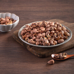 Cashew nuts with peel in a plate on wooden tray.
