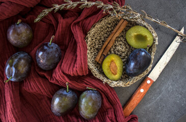 Fresh plums, cinnamon, knife and rosemary on a table. Red textured cotton drapery on background. 