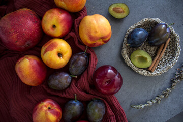 Flat lay photo of fresh fruits. Juicy nectarines, plums, cinnamon, rosemary and kitchen knife on a table. Vibrant colors of garden fruits. 