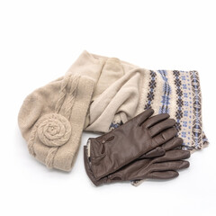 Women's accessories for winter and autumn. Knitted beige hat, warm scarf with an ornament. Brown gloves made of genuine leather with a fur lining. Isolated over white background.