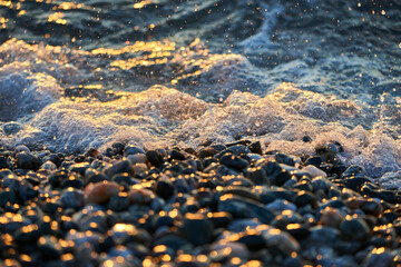 detail of the foam of a wave on the pebbles of the beach in the warm hours of sunris