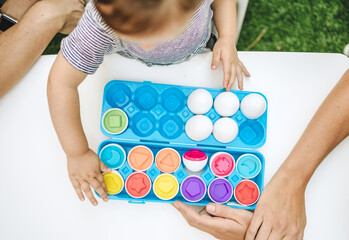A girl playing with her parents with colored educational toys and figures in their home garden