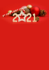 Vertical Christmas card with 2021 numbers in the foreground and New Year's balls, pine cones and a candy cane in the background. New Year's layout with a red background, Side view. Copyspace