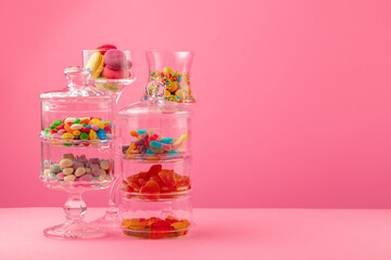 Glass containers with candies against pink background