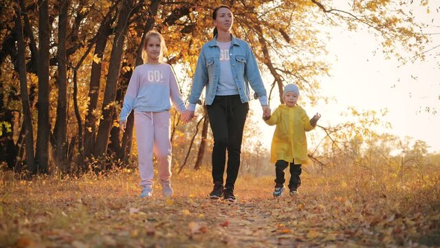 Mother and two children walking in the park and enjoying the beautiful autumn nature. Happy family on autumn walk.