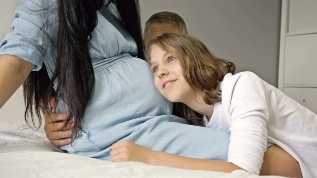 Teenager boy listens with admiration to the movement of the baby in the belly of a pregnant mother.