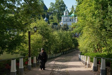 Pechory. Holy Dormition Pskov-Pechersky Monastery. A monk in black clothes walks along the road from the monastery on a summer day