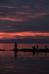 Beautiful selective focus image of dramatic sunset with calm water and two people fishing on a pier