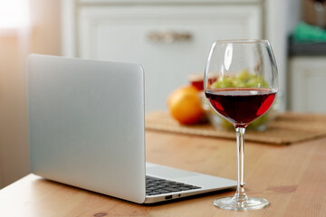 Laptop and glass of red wine on wooden kitchen table