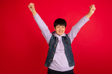 Happy winner. Portrait of senior woman in stylish outfit, attire isolated on red studio background....