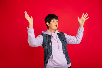 Shocked, astonished. Portrait of senior woman in stylish outfit, attire isolated on red studio...