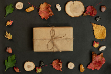 Gift box and autumn maple leaves, cones, acorns, stones on a black background, creative flat lay, top view, copy space. Seasonal autumn concept. Autumn fallen leaves on black background. 