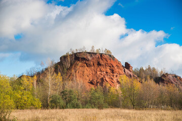 Red mountains with autumn trees and blue cloudy sky. Colored waste heaps after extracting coal from...