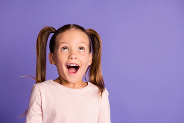 Photo of amazed pretty little girl wear sweatshirt look up empty space isolated on purple color background