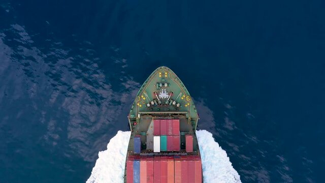 Luftaufnahme des Bug eines Frachters belden mit Containern bei voller Fahrt &uuml;ber blauem Meer
