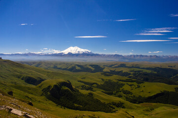 An excellent view from the plateau to the extinct volcano and the snowy peak of Mount Elbrus. Below is a green gorge