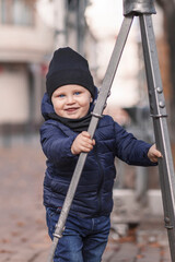 A little boy is holding a metal tripod. A child in warm clothes smiles