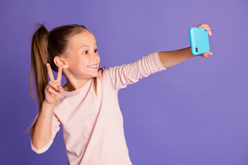 Photo of brown haired tails little girl wear sweater hold phone make selfie v-sign isolated on...