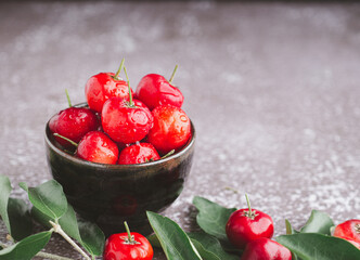 Ripe red cherries in a ceramic dish with leaves on a wooden table. Space for text. Sweet organic berries. Concept of healthy fruits