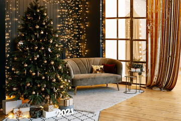 Christmas tree in the interior of the living room, decorated with gifts and garlands. Stylish interior in dark and gold tones, decorated for the New Year.
