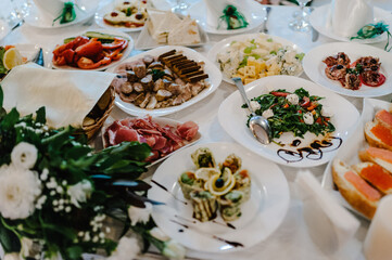 Serves dinner on a festive table. Food, Salads, Meat, Fish Meals. Festive table at wedding banquet. Decor. Details.
