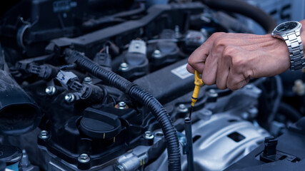 A young professional mechanic holds the dipstick of a car engine. Check his car's oil level