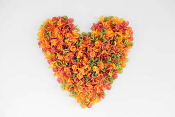 Multicolored pasta scattered on a white background in the shape of a heart. Top view. Copy, empty space for text
