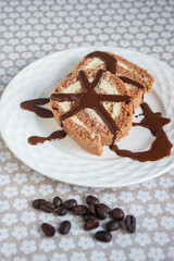 Coffee Swiss roll two slices drizzled with dark chocolate on glass decorated white plate, spilled fresh coffee beans