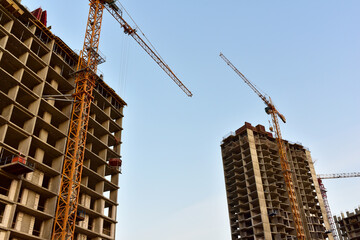 Tower cranes working at construction site against blue sky. Crane lifting a concrete bucket. Construction process of the new residential buildings. Transportation blocks and pouring of the cement mix