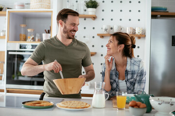 Fototapeta na wymiar Husband and wife making pancakes at home. Loving couple having fun while cooking