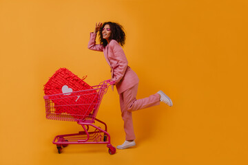 Good-humoured girl in pink pants enjoying shopping. Indoor shot of glad lady with supermarket cart.