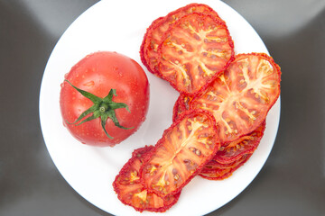 Fresh red tomato and dried tomato slices on a plate. Vitamin vegetable food