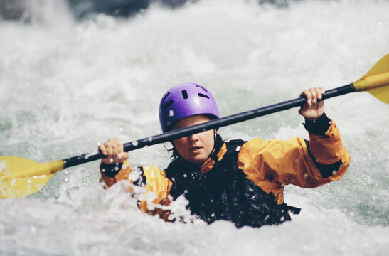 Female whitewater kayaker paddling rapids and surf on a fast flowing river.