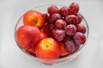 Naklejka na ściany i meble Glass bowl with fresh grapes and nectarines on white table, closeup