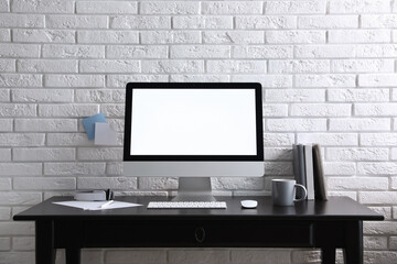 Fototapeta premium Comfortable workplace with modern computer on black table near white brick wall. Space for text