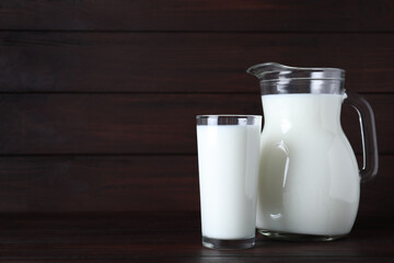 Jug and glass with fresh milk on wooden table. Space for text