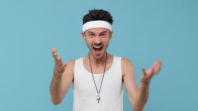 Perplexed irritated young fitness man with thin skinny body sportsman in headband shirt isolated on pastel blue background. Workout gym sport motivation concept. Spreading hands screaming swearing